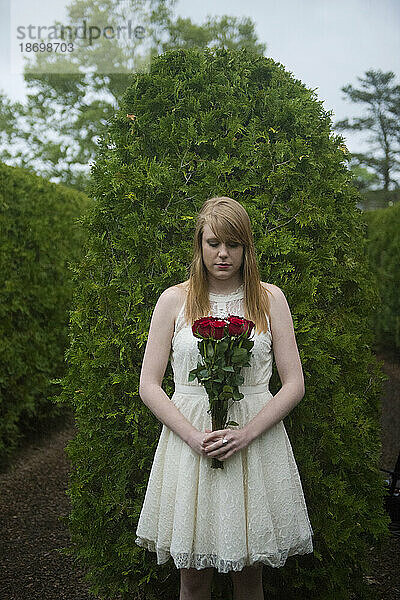Junge Frau steht mit einem Strauß roter Rosen in einem Gartenbereich; Luray  Virginia  Vereinigte Staaten von Amerika