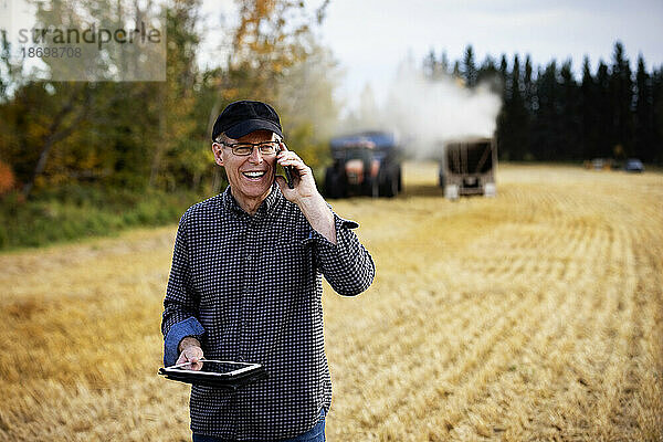 Landwirt nutzt ein Tablet  um seine Ernte zu verwalten  und telefoniert mit Erntemaschinen im Hintergrund; Alcomdale  Alberta  Kanada