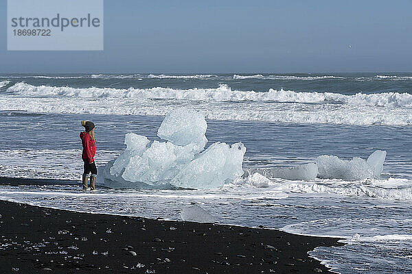 Blick auf eine Frau  die am Strand am Wasser steht und die Eisberge entlang der Südküste Islands bewundert; Jökulsárlón  Südisland  Island