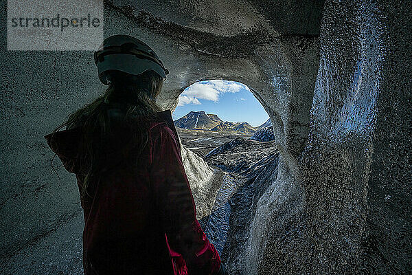 Blick durch eine Eishöhle auf eine Frau  die auf einer Reise in Island einen Gletscher erkundet; Vik  Südisland  Island