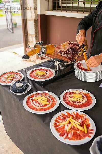 Detail eines Mannes beim Schneiden von iberischem Schinken bei einer Hochzeit oder Veranstaltung. Service einer Person  die ein Stück Schinken schneidet. Koch oder Cutter mit einem Messer. traditionelle spanische Küche