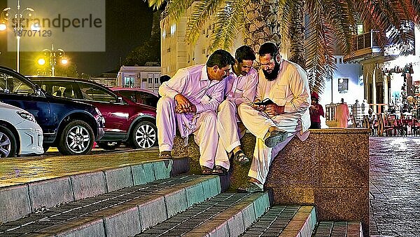 Drei Männer schauen auf Handy  traditionell  Kleidung  Abend  Licht  Muskat  Oman  Schlachtung  Asien