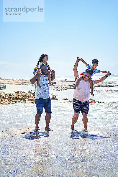 Schwules männliches Paar trägt Kinder auf Schultern  sonnige Meeresbrandung