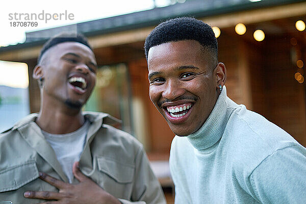 Porträt eines glücklichen jungen schwulen männlichen Paares  das auf der Terrasse lacht