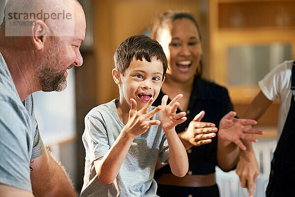 Porträt eines glücklichen Jungen mit Down-Syndrom  der mit der Familie klatscht
