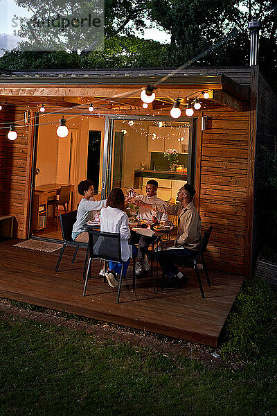 Schwule Paare genießen das Abendessen am Tisch auf der Terrasse mit Lichterketten