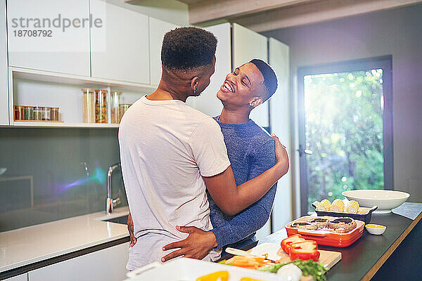 Fröhliches  liebevolles junges schwules Männerpaar  das sich zu Hause umarmt und kocht