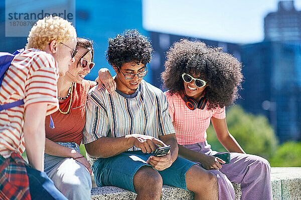 Junge Freunde nutzen Smartphones in der sonnigen Stadt