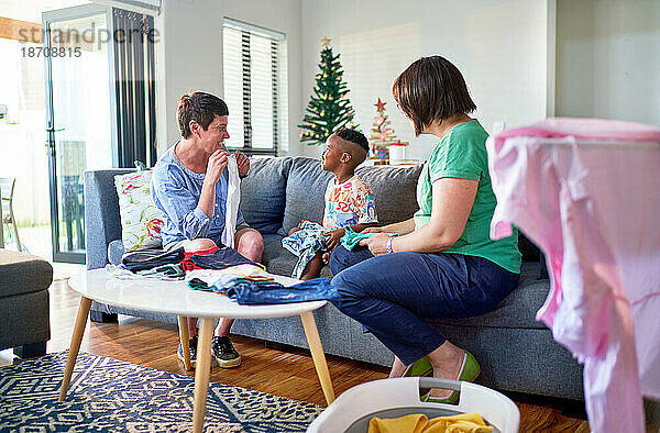 Lesbisches Paar und Sohn falten Wäsche auf dem Sofa im Wohnzimmer