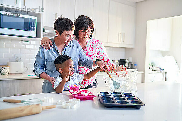 Glückliches lesbisches Paar und Sohn backen gemeinsam Cupcakes in der Küche