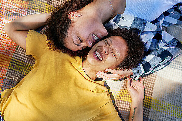 Blick von oben: glückliches lesbisches Paar  das auf einer Decke lacht