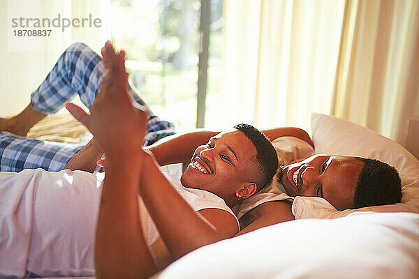 Fröhliches  liebevolles junges schwules männliches Paar  das Händchen auf dem Bett hält
