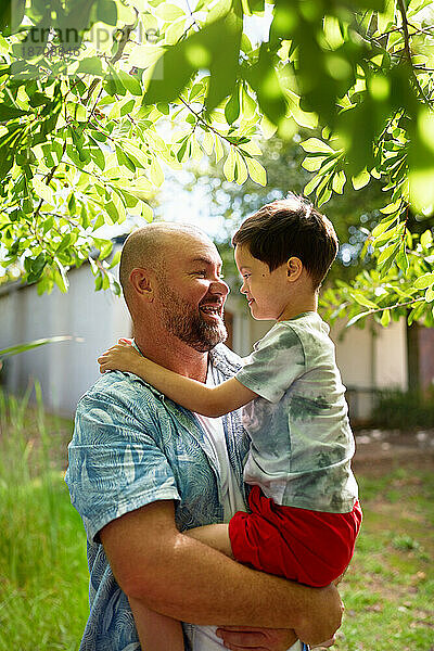 Glücklicher Vater hält süßen Sohn mit Down-Syndrom im Hinterhof