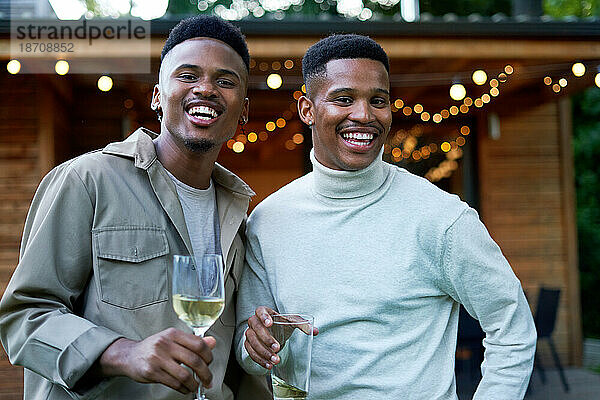 Porträt eines glücklichen jungen schwulen männlichen Paares  das im Hinterhof trinkt