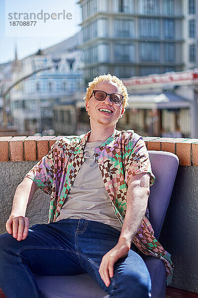 Porträt eines glücklichen jungen Albino-Mannes  der auf dem sonnigen Dach der Stadt sitzt