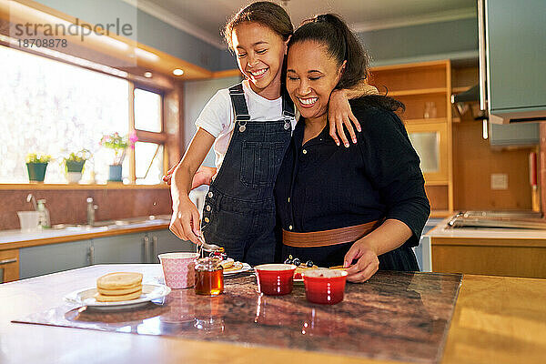 Glückliche Mutter und Tochter essen Pfannkuchen in der Morgenküche