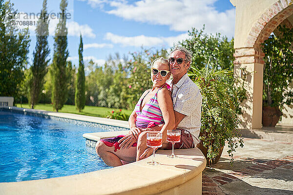 Porträt eines glücklichen älteren Paares  das sich im sonnigen Sommerschwimmbad entspannt