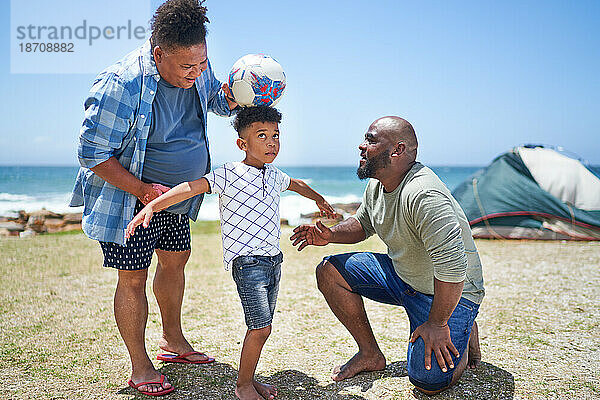 Schwules männliches Paar und Sohn spielen mit Fußball am sonnigen Strand