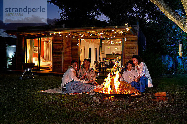 Glückliche schwule Paare rösten Marshmallows an der Feuerstelle im sommerlichen Hinterhof