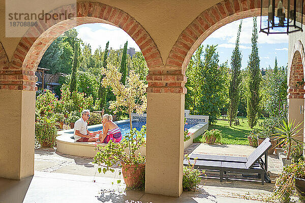 Älteres Paar unterhält sich und entspannt sich am Pool der sonnigen Villa