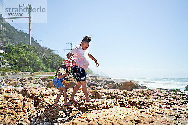 Vater und Tochter laufen barfuß auf Felsen am sonnigen Strand