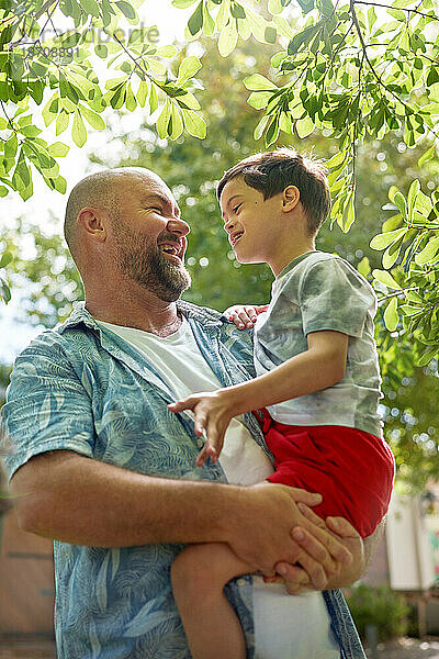 Glücklicher Vater hält seinen süßen Sohn mit Down-Syndrom unter dem Baum