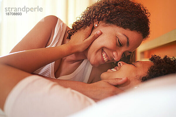 Nahaufnahme eines glücklichen  liebevollen lesbischen Paares  das von Angesicht zu Angesicht auf dem Bett lächelt