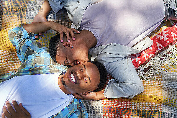 Glückliches junges schwules männliches Paar  das sich auf einer Decke küsst
