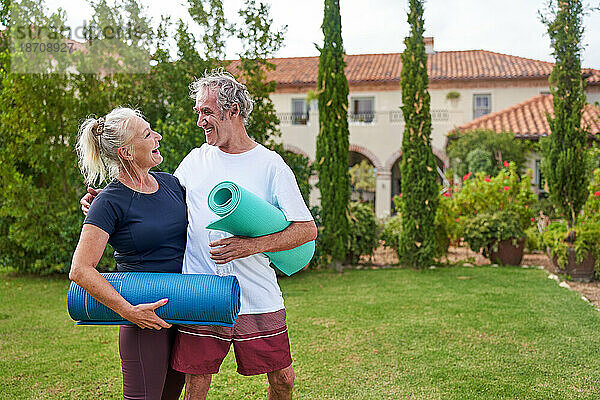 Glückliches älteres Paar mit Yogamatten im Garten der Villa