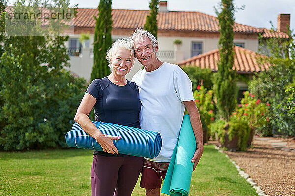 Porträt eines glücklichen  aktiven Seniorenpaares mit Yogamatten im Garten der Villa