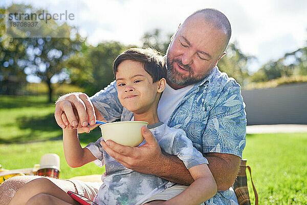 Porträtvater füttert süßen Sohn mit Down-Syndrom im Sommerpark