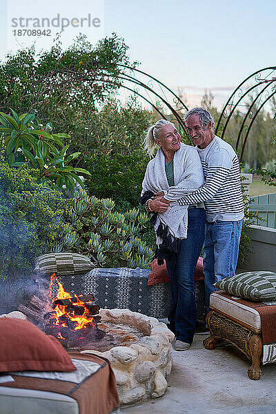 Glückliches älteres Paar umarmt sich an der Feuerstelle auf der Gartenterrasse