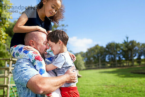 Vater hält und trägt Tochter und Sohn mit Down-Syndrom im Park