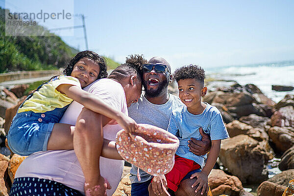 Glückliches schwules männliches Paar und Kinder  die auf sonnigen Strandfelsen lachen