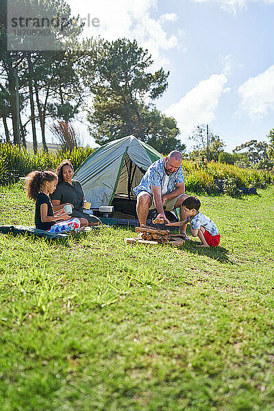 Fröhliches Familiencamping  Brennholz vor dem Zelt im sonnigen Gras stapeln