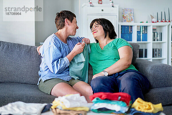 Glückliches lesbisches Paar redet und faltet Wäsche auf dem Sofa im Wohnzimmer