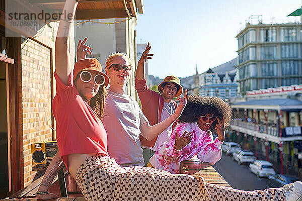 Porträt glücklicher junger Freunde  die auf einem sonnigen städtischen Balkon gestikulieren