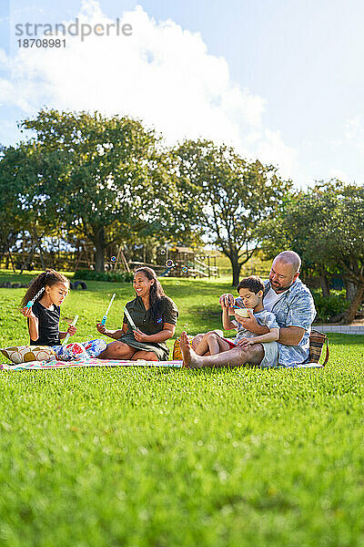 Familie isst und bläst Seifenblasen auf dem Rasen im Sommerpark