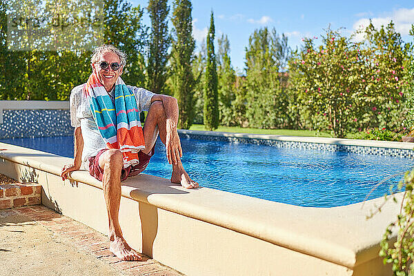 Porträt eines glücklichen älteren Mannes  der sich am sonnigen Swimmingpool entspannt