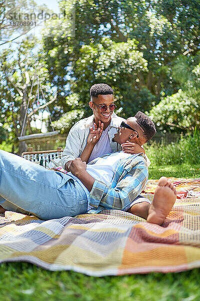 Glückliches junges schwules Männerpaar kuschelt auf Picknickdecke im Park