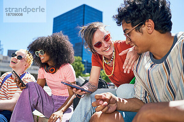 Fröhliche junge Freunde  die in der sonnigen Stadt ihr Smartphone nutzen