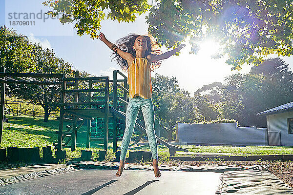Unbekümmertes Mädchen springt auf Trampolin im sonnigen Hinterhof