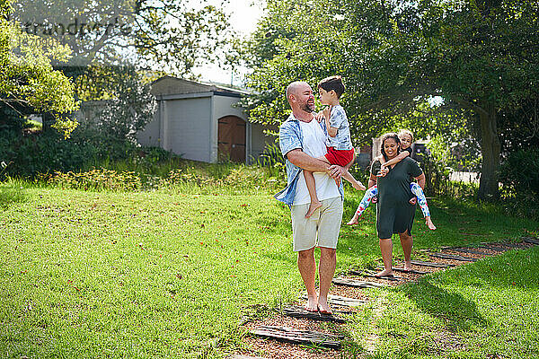 Glückliche Eltern tragen Tochter und Sohn auf dem Weg im sonnigen Hinterhof