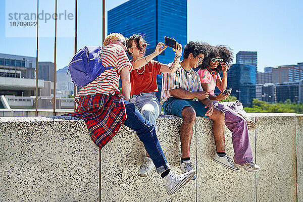 Junge Freunde hängen herum und nutzen Smartphones in der sonnigen Stadt