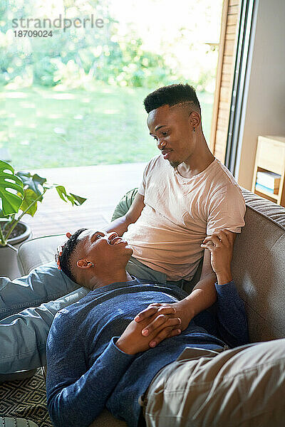 Liebevolles junges schwules männliches Paar  das zu Hause auf dem Sofa kuschelt und redet