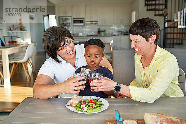 Glückliches lesbisches Paar und Sohn  die am Esstisch mit Trinkgläsern anstoßen