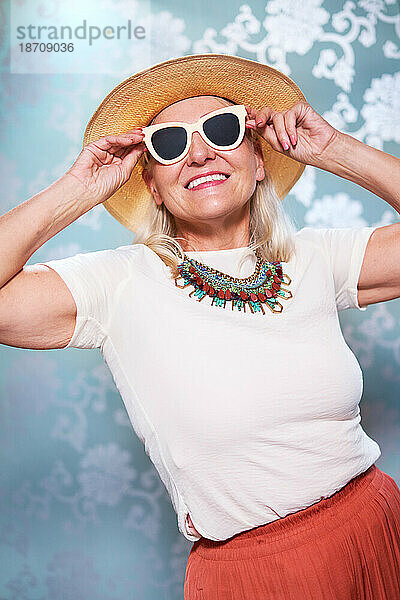 Porträt einer unbeschwerten älteren Frau mit Sonnenbrille und Strohhut