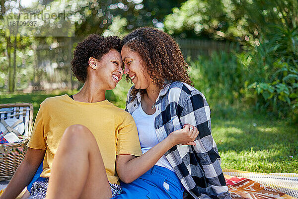 Fröhliches  liebevolles lesbisches Paar kuschelt auf Picknickdecke im Park