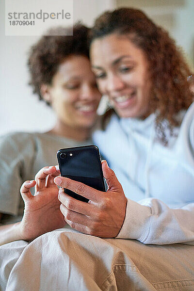 Glückliches lesbisches Paar  das zu Hause gemeinsam sein Smartphone nutzt