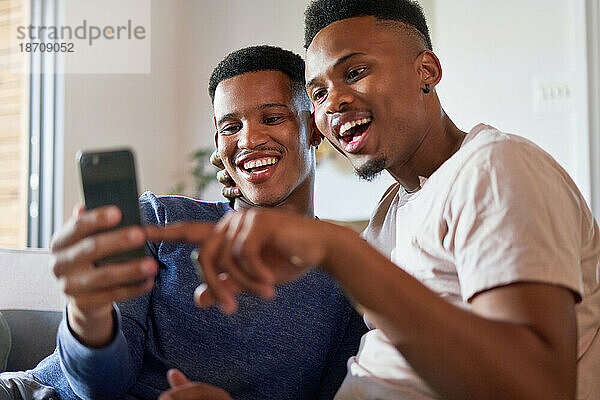 Glückliches junges schwules männliches Paar  das zu Hause sein Smartphone nutzt